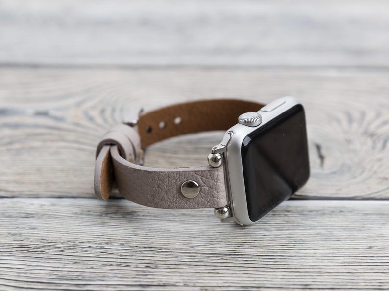 May include: A silver Apple Watch with a light gray leather band. The band has a textured finish and silver metal accents.