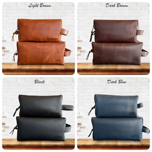 May include: Four leather toiletry bags in light brown, dark brown, black, and dark blue. Each bag has a zipper closure, a side handle, and a wrist strap. The light brown bag is labeled "Alexander" and "JKL". The dark brown bag is labeled "HS" and "YOUR LOGO HERE". The black bag is labeled "Hector" and "Drew". The dark blue bag is labeled "NB" and "HFG".
