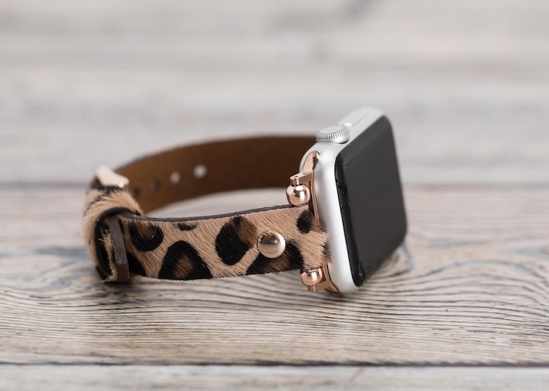 May include: A brown and black leopard print leather watch band with rose gold accents. The band is designed for an Apple Watch.