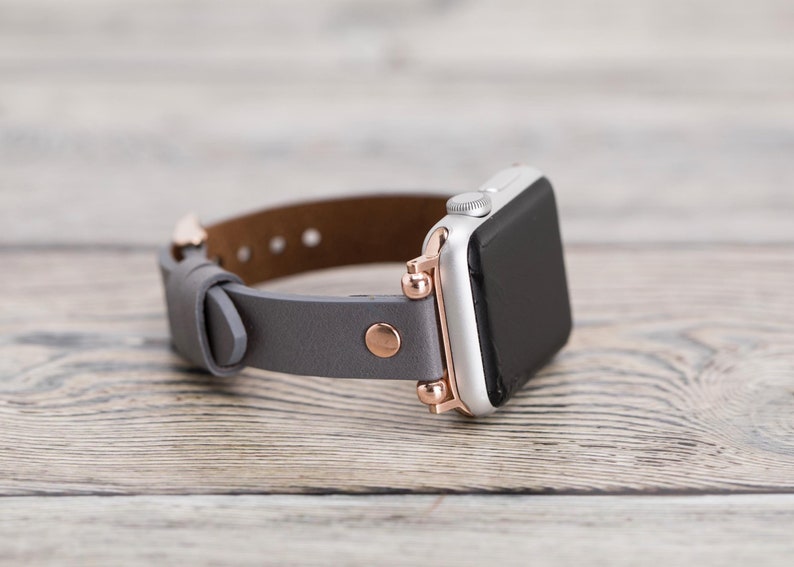 May include: A gray leather watch band with rose gold accents and a silver Apple Watch.