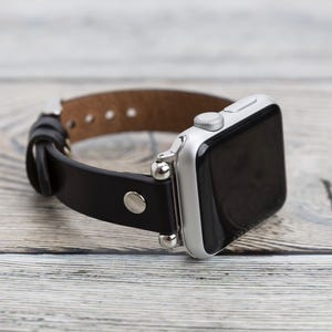 May include: A black leather watch band with silver accents and a silver Apple Watch.