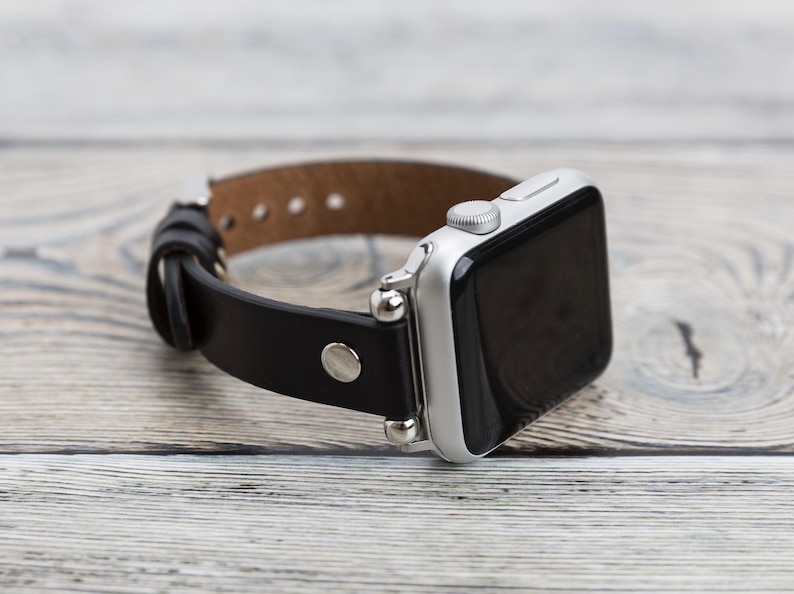 May include: A black leather watch band with silver accents and a silver Apple Watch.