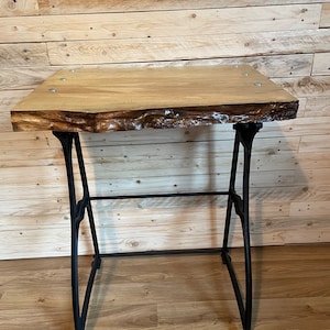 May include: A wooden table top with a live edge and a black metal base. The table top is made of light wood with a natural finish. The base is made of sturdy metal with a black finish.