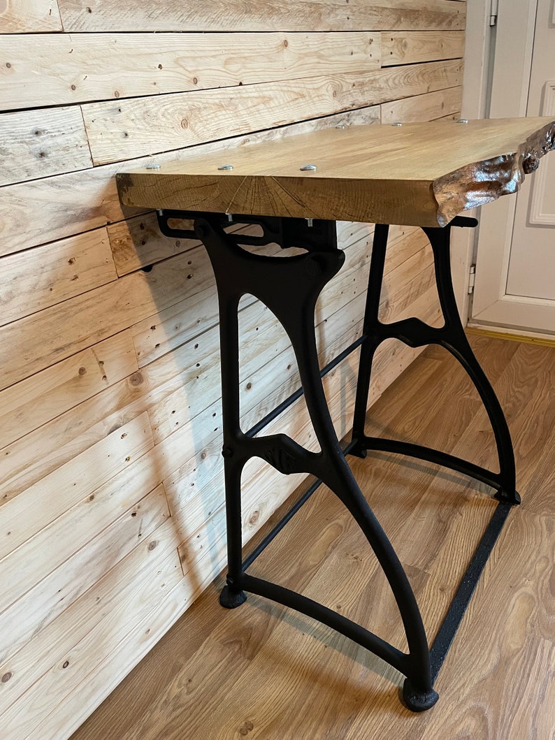 May include: A wooden table top with a live edge sits on top of black metal industrial style legs. The table is mounted to a wall.