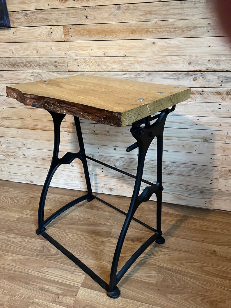 May include: A wooden table top with a live edge sits on a black metal adjustable base. The table top is made of light wood and has a natural finish. The base is made of cast iron and has a black finish.
