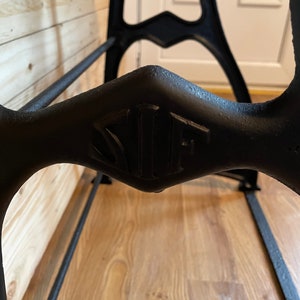 May include: Close-up of a black metal industrial table base with a diamond-shaped detail featuring the letters "NUF" embossed in the center.