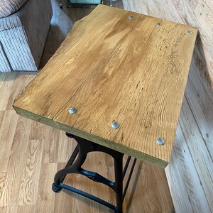 May include: A rustic wooden table top with a black metal base. The table top is made of reclaimed wood and has a natural finish. The base is made of cast iron and has a black finish. The table is perfect for a small space and can be used as a side table, coffee table, or end table.