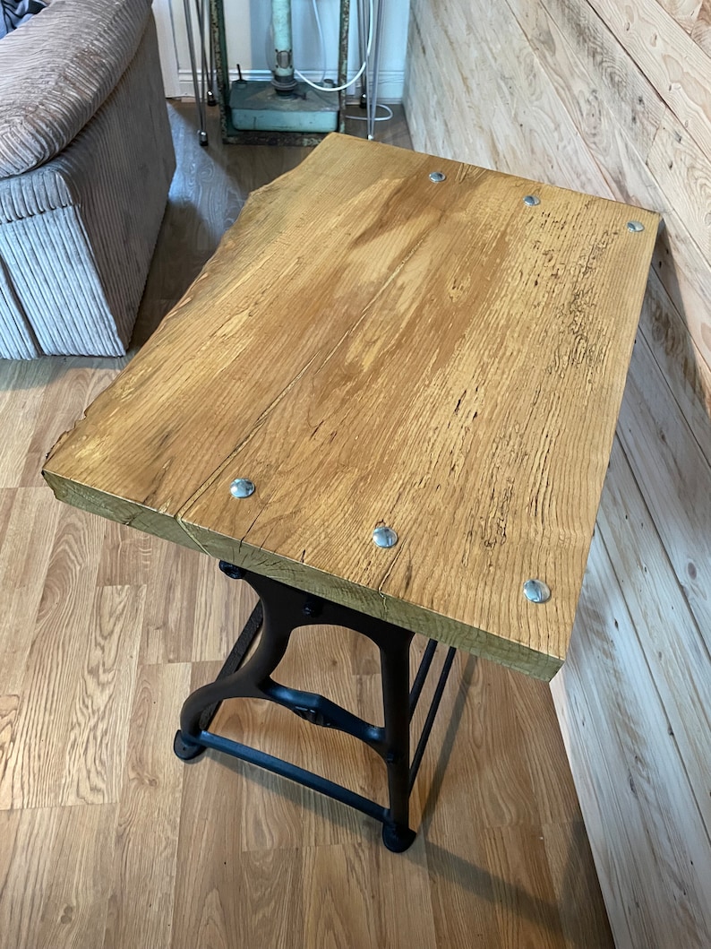 May include: A rustic wooden table top with a black metal base. The table top is made of reclaimed wood and has a natural finish. The base is made of cast iron and has a black finish. The table is perfect for a small space and can be used as a side table, coffee table, or end table.