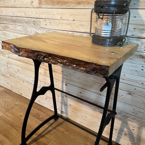 May include: A rustic wooden table with a live edge top and black metal legs. The table is topped with an antique brass lantern.