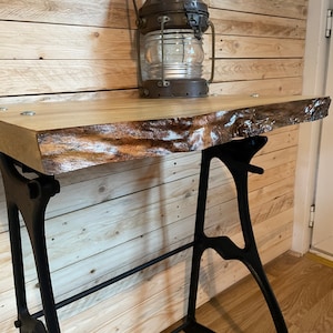 May include: A rustic wooden table with a live edge top and black metal legs. The table is decorated with an antique oil lamp.