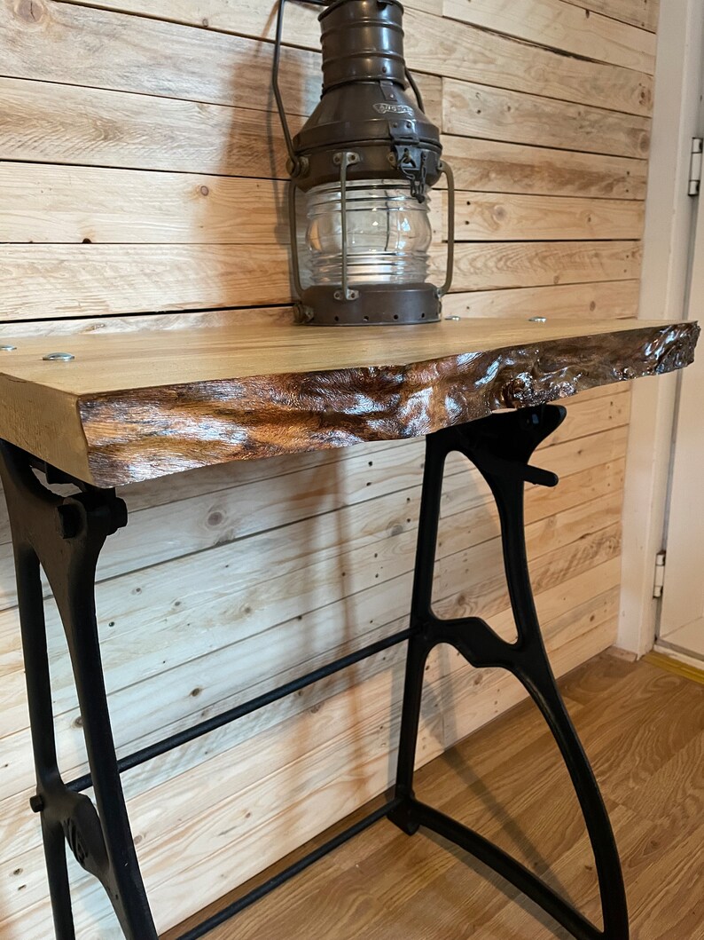 May include: A rustic wooden table with a live edge top and black metal legs. The table is decorated with an antique oil lamp.