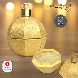 May include: Gold-colored, paper Christmas ornament with a floral pattern. The ornament is in three pieces, with the top and bottom halves separated, and the middle section open. The text "SVG Cut File" is visible.