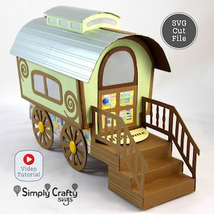 Puede incluir: Una manualidad de papel de una caravana gitana en tonos verdes, marrones y plateados. La caravana presenta remolinos decorativos, una puerta, ventanas y una pequeña escalera. Las ruedas son amarillas y marrones. Incluye el texto "SVG Cut File".