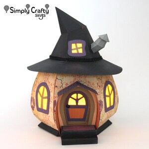 Peut inclure: Une maison de sorci&egrave;re en papier avec un chapeau pointu noir, une chemin&eacute;e et des fen&ecirc;tres avec des lumi&egrave;res qui brillent. La maison est d&eacute;cor&eacute;e d'un motif floral et a une petite porte avec une poign&eacute;e de porte brune.