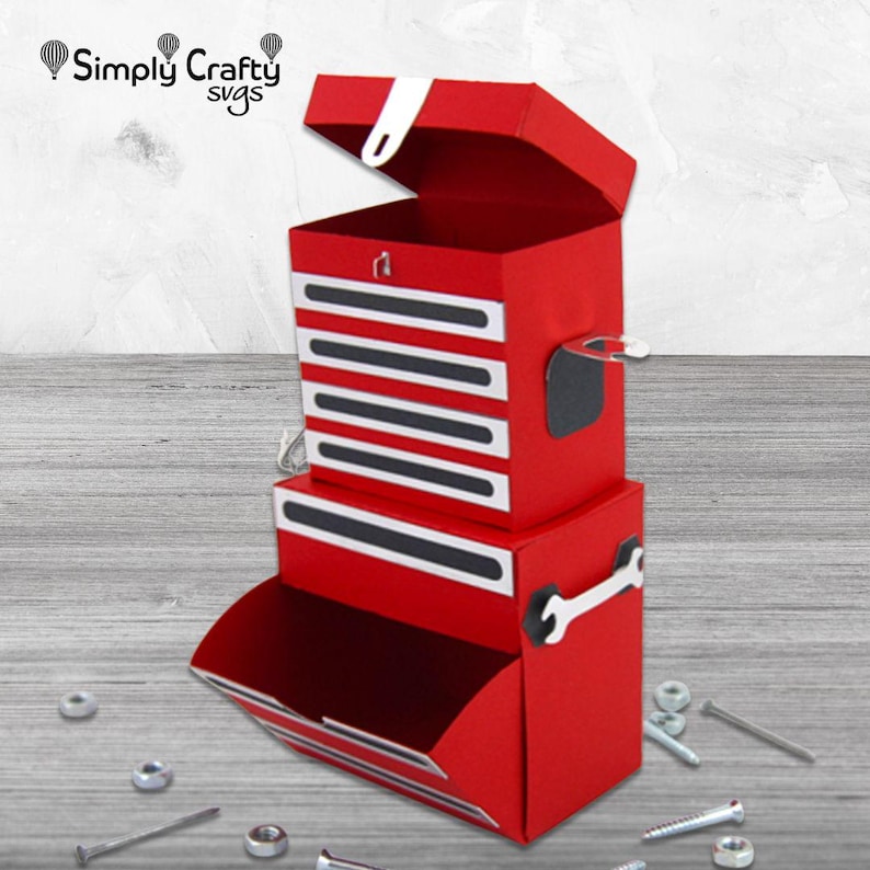 May include: A red paper toolbox with white detailing and a hinged lid. The toolbox features multiple drawers and a wrench-shaped cutout. The top of the toolbox has the text "Simply Crafty svgs".