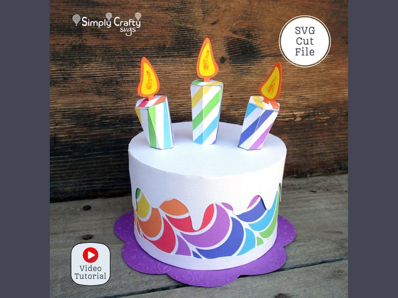 May include: A colourful papercraft birthday cake with three striped candles and a purple base. The cake has a rainbow swirl design and the text "SVG Cut File" is visible in the top right corner.