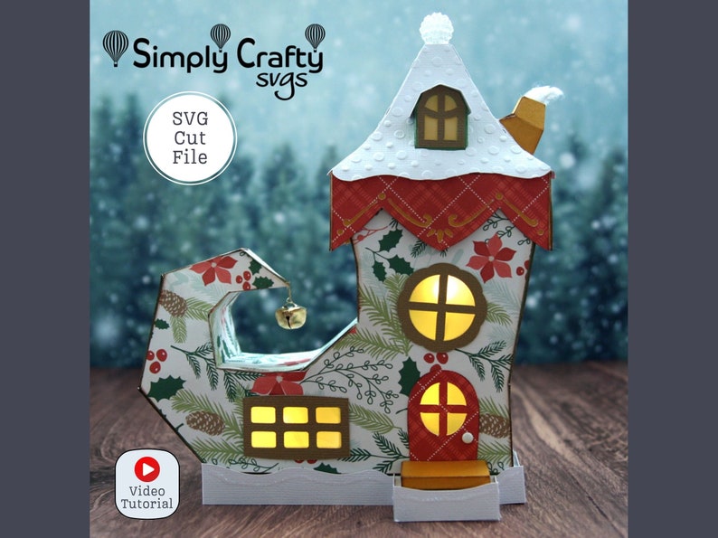 May include: A festive elf shoe house with a snowy roof, red and green accents, and a lit window. The house is decorated with holly, pine cones, and poinsettias. The image includes the text "Simply Crafty svgs" and "SVG Cut File".