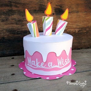 May include: A pink and white paper cake with three striped candles and the words "Make a Wish" on the side.