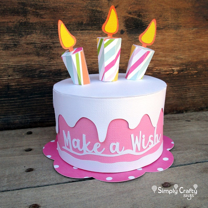 May include: A pink and white paper cake with three striped candles and the words "Make a Wish" on the side.