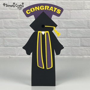 Pode incluir: Um chap&eacute;u e uma beca de gradua&ccedil;&atilde;o pretos com uma borla amarela e detalhes roxos. O chap&eacute;u tem um c&iacute;rculo preto no topo. A beca tem uma faixa roxa com detalhes amarelos. As palavras "CONGRATS" est&atilde;o escritas em letras amarelas sobre um fundo roxo acima do chap&eacute;u.