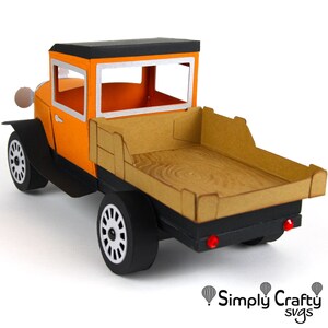 Peut inclure: Un camion jouet vintage orange et noir avec une benne en bois. Le camion a un toit noir et un cadre de fen&ecirc;tre argent&eacute;. Le camion est sur un fond blanc.