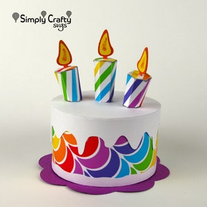 May include: A colourful papercraft birthday cake with three striped candles and a purple base. The cake is decorated with a rainbow swirl pattern.