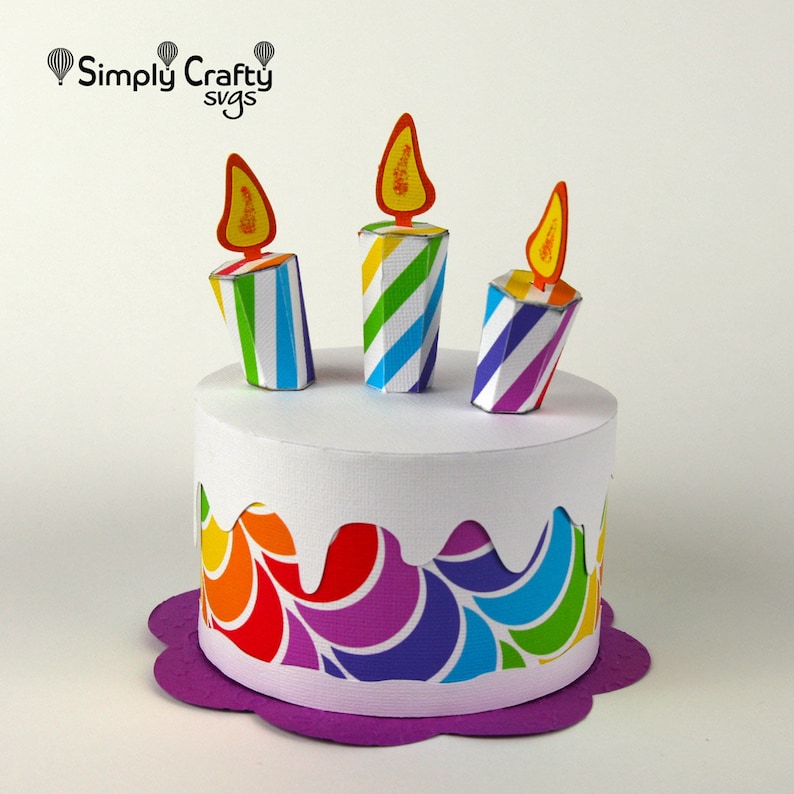 May include: A colourful papercraft birthday cake with three striped candles and a purple base. The cake is decorated with a rainbow swirl pattern.