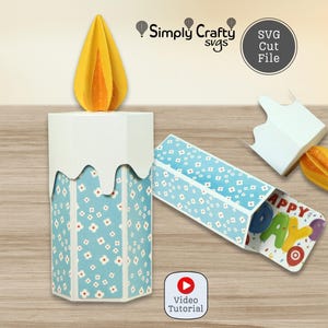 Puede incluir: Una caja de manualidades de papel con forma de vela, patrón floral azul y blanco, llama de papel amarilla y diseño de goteo blanco. La caja tiene un cajón deslizante que revela el texto HAPPY DAY. Incluye Simply Crafty SVGs y Video Tutorial.