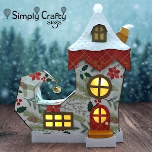 May include: A festive elf shoe house with a red roof, white snow, and a bell hanging from the toe. The house has windows with glowing lights and a red door. The shoe is decorated with a green and white Christmas pattern.