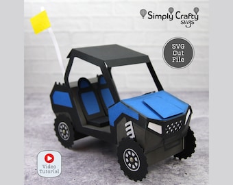 May include: A blue and black papercraft model of a side-by-side off-road vehicle with a roll cage. The model has a yellow flag attached to the top. The text "SVG Cut File" is visible in the image.