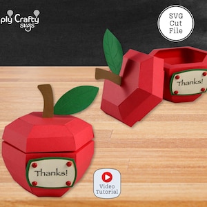 May include: A red apple-shaped paper box with a brown stem and green leaf. The box features a cream-coloured label with the text "Thanks!" attached by four red studs. One box is closed, and another is open, showing the hollow interior structure.
