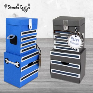 May include: Two stacked paper toolbox-shaped gift boxes. One is blue with white and black accents, the other is grey with white and blue accents. The grey box has a tag that says "Happy Birthday".
