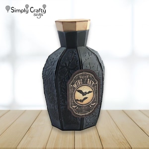 May include: A black, multi-faceted bottle with a tan hexagonal lid. The bottle features a textured surface and a central label with a cream-colored circular background, two black bat silhouettes, and the text "DRIED WING OF BAT".