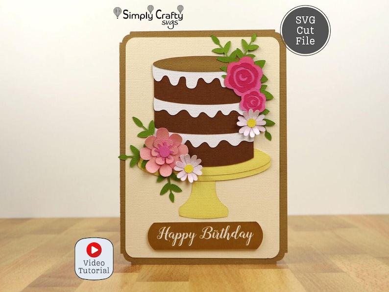 May include: A handmade birthday card featuring a chocolate cake with white frosting, adorned with pink and white paper flowers and green leaves. The card has a beige background and a brown border, with the words "Happy Birthday".