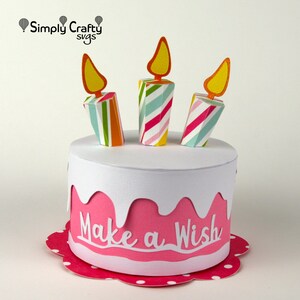 May include: A pink and white paper cake with three colourful striped candles and the words "Make a Wish" on the side.