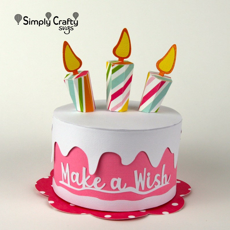 May include: A pink and white paper cake with three colourful striped candles and the words "Make a Wish" on the side.