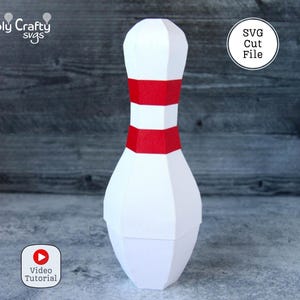 May include: A white paper bowling pin with a red stripe around the middle. The pin is a 3D SVG cut file. The image also includes the text "SVG Cut File" and "Video Tutorial".