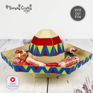 May include: A colorful paper sombrero-shaped candy holder with a red, yellow, and blue design. The tray is filled with wrapped candies, including Smarties. The image includes the text "Simply Crafty Svgs" and "SVG Cut File".