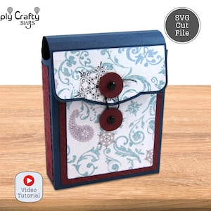 May include: A handmade paper box with a flap closure, featuring a navy blue top and burgundy sides. The front panel is white with a teal and purple floral pattern, secured by two burgundy buttons. The box is labelled "SVG Cut File".