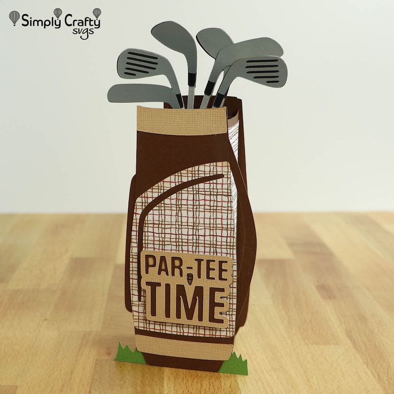 May include: A brown and tan golf bag with a plaid pattern and a green grass base. The bag is filled with gray golf clubs and has a brown sign that says "Par-Tee Time".