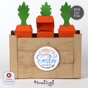 Può includere: Una scatola artigianale di carta con tre contenitori a forma di carota arancione e cime verdi a forma di foglia. La scatola ha un design a venature del legno e un'etichetta circolare con la scritta "Carrots for the Easter Bunny."
