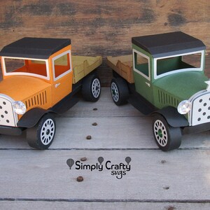 Peut inclure: Deux camions jouets de style vintage, l'un orange et l'autre vert, avec des roues noires et une benne en bois. Les camions se font face sur une surface en bois. Le texte "Simply Crafty svgs" est visible sous les camions.