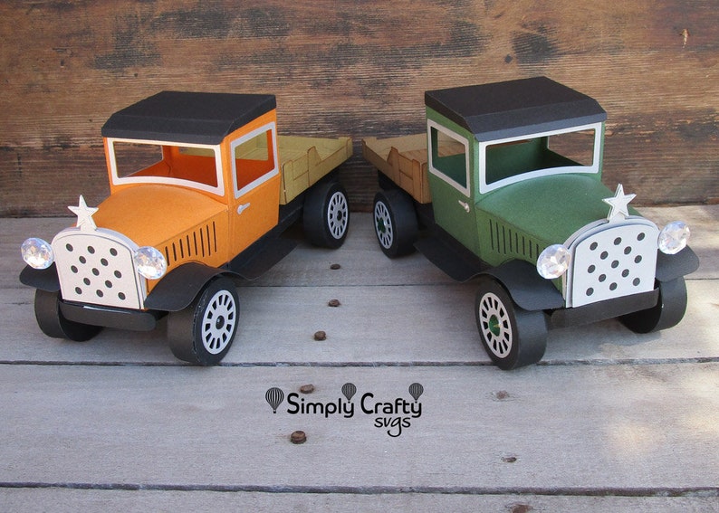 Peut inclure: Deux camions jouets de style vintage, l'un orange et l'autre vert, avec des roues noires et une benne en bois. Les camions se font face sur une surface en bois. Le texte "Simply Crafty svgs" est visible sous les camions.