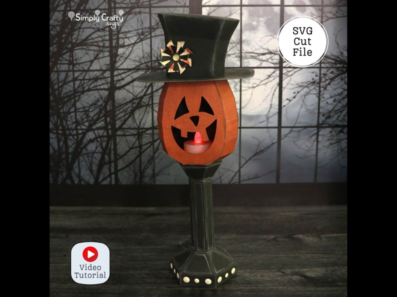 May include: A papercraft jack-o'-lantern with a top hat and a lit candle inside. The jack-o'-lantern is on a black stand with a decorative base. The background is a dark window with a blurry image of trees and a moon. The text "SVG Cut File" is in a white circle on the right side of the image. The text "Video Tutorial" is in a red circle with a play button on the left side of the image.