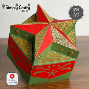May include: A geometric papercraft star-shaped box in red, green, and gold glitter. The box has a star on top and decorative cutouts. The text "SVG Cut File" is in a circle. The text "Video Tutorial" is in a circle.