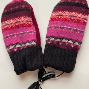 May include: A pair of pink and burgundy knit mittens with black cuffs and a black string tie.