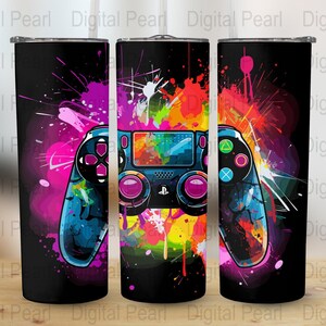 May include: A black tumbler with a colorful abstract design featuring a video game controller. The controller is blue, black, and white with pink buttons. The background is a mix of pink, blue, yellow, orange, and green.