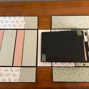Op de afbeelding: Een meerdelig plakboekalbum met diverse patronen in saliegroen, zachtroze en wit. Het open album toont verschillende zwarte kartonnen pagina's en vakjes, voorzien van decoratieve blad-, ruit- en bloemenprints.
