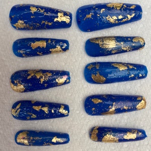 May include: Ten blue and gold press-on nails with a gold foil design.