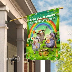 Pode incluir: Uma bandeira verde, branca e dourada do Dia de São Patrício com três ovelhas de desenho animado segurando canecas de cerveja. A bandeira diz "Irish ewe # happy St. P*trick's Day!" com um arco-íris e trevos.